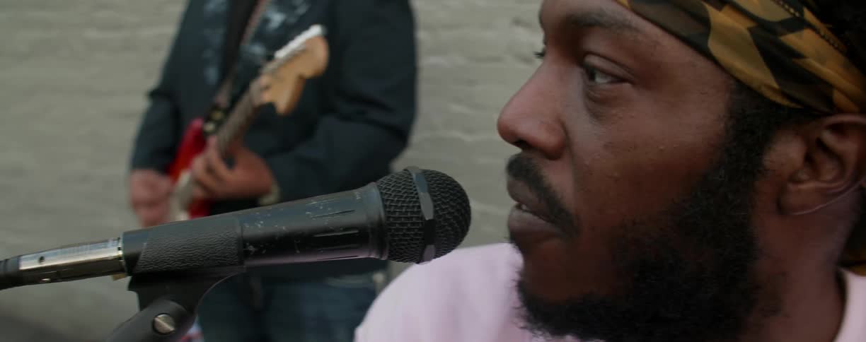 A man is singing into a microphone as someone plays guitar