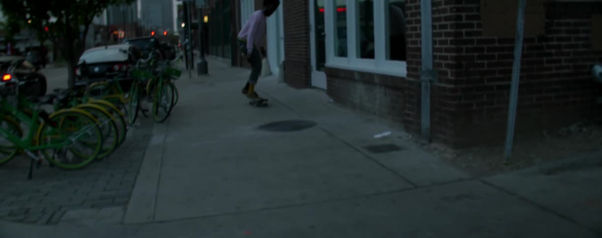 A man riding a skateboard jumps a manhole cover on a sidewalk at dusk