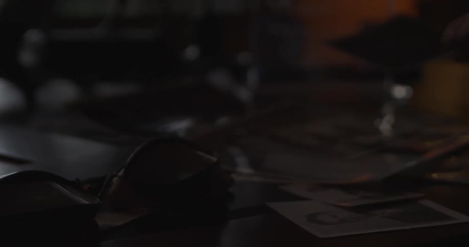Closeup pan across old photos and mementos on a desk toward a person standing holding a photo