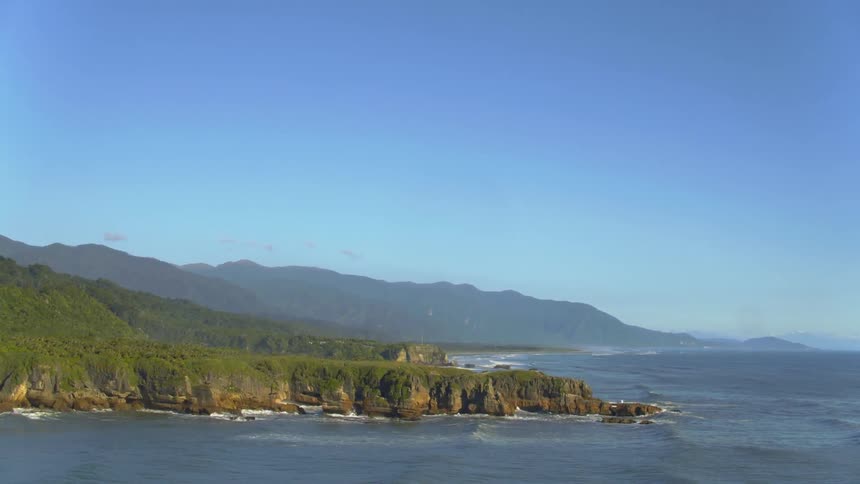 A helicopter is flying over the ocean looking at a green cliff