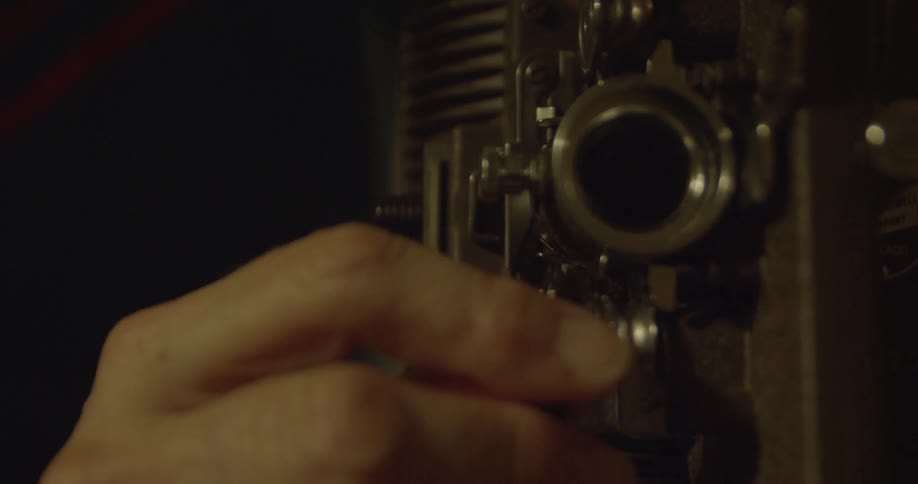 A woman's hand threads film through an old projector