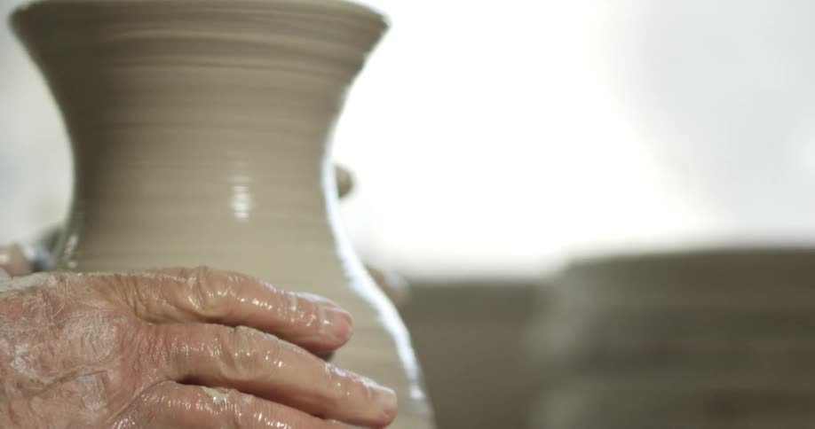 A pair of old hands shape a wet clay vessel