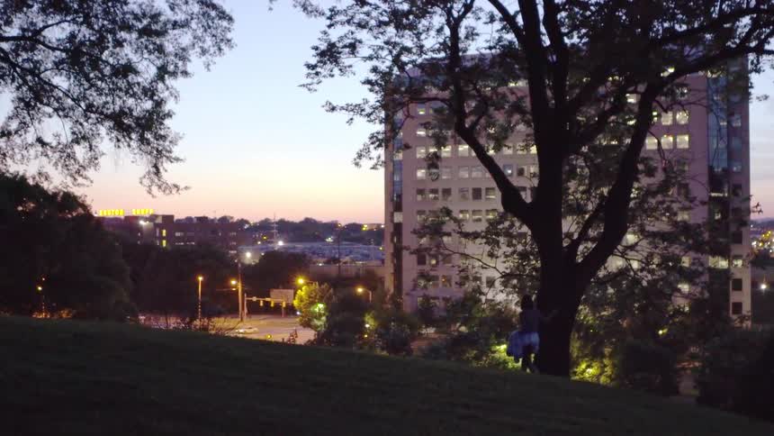 A woman walks up a grassy hill in a city