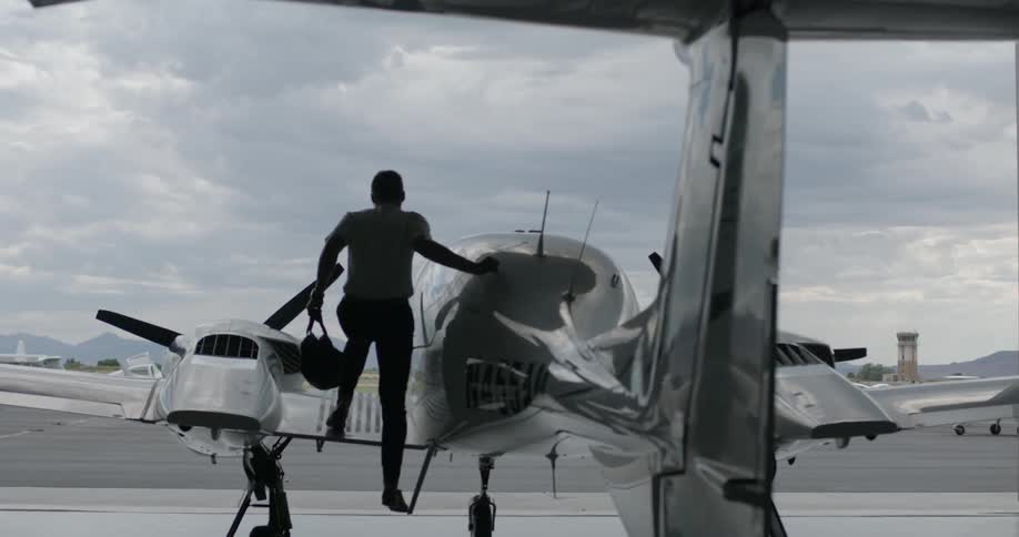 A pilot carrying a bag climbs up onto a small plane