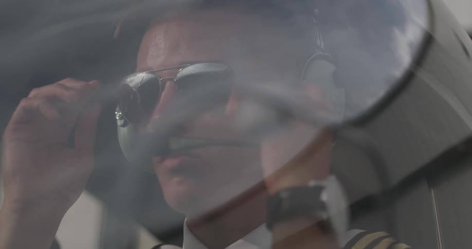 A pilot is putting on his sunglasses while sitting in a small plane