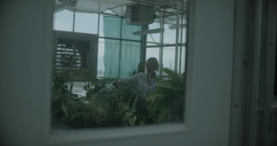 A lady is spraying her plants with water inside a greenhouse