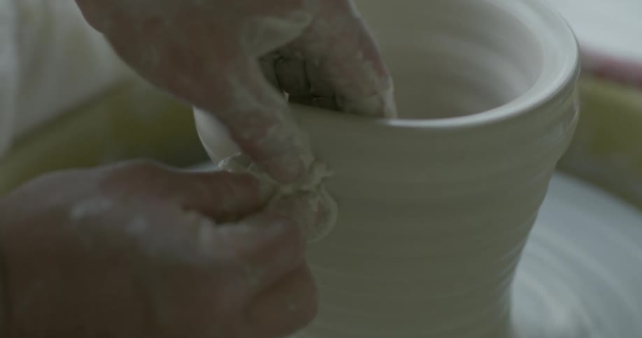 Person molding clay as it spins on a spinner