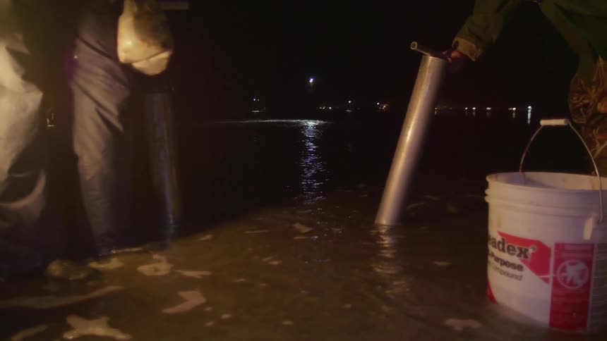People are digging and using buckets by the shore at night