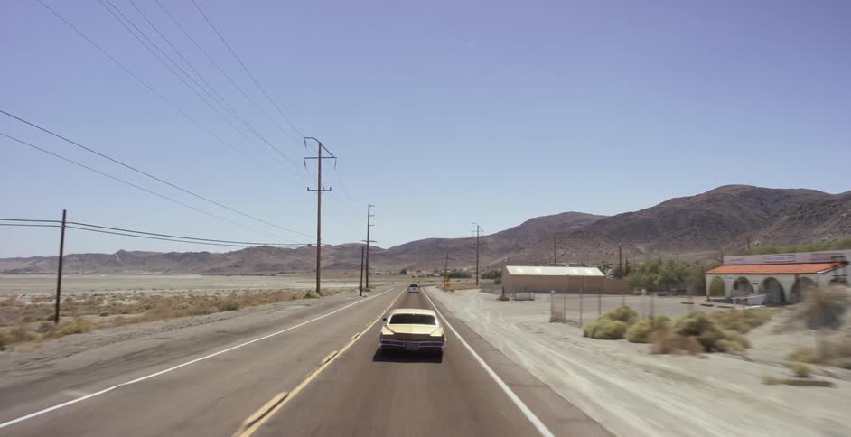 A classic car is driving down a desert road