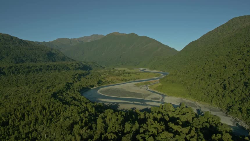 A river is flowing through a forest in a mountain valley on a sunny day