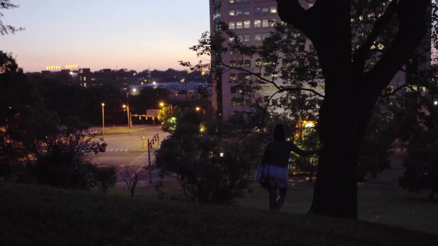 Woman stands in city park at dusk