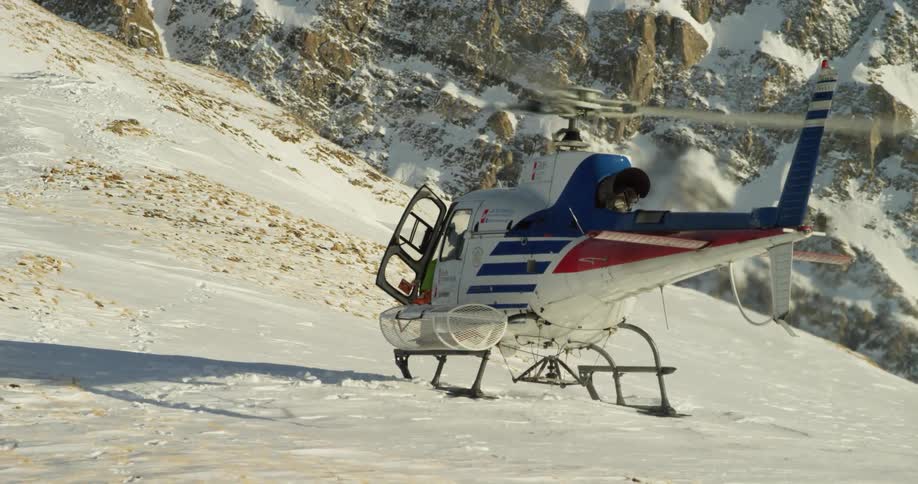 A man in a green suit climbs into a helicopter on the side of a snowy hill