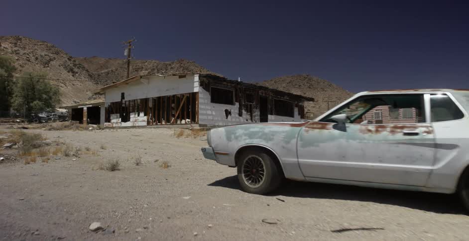An old car is sitting next to a collapsing abandoned building in the desert