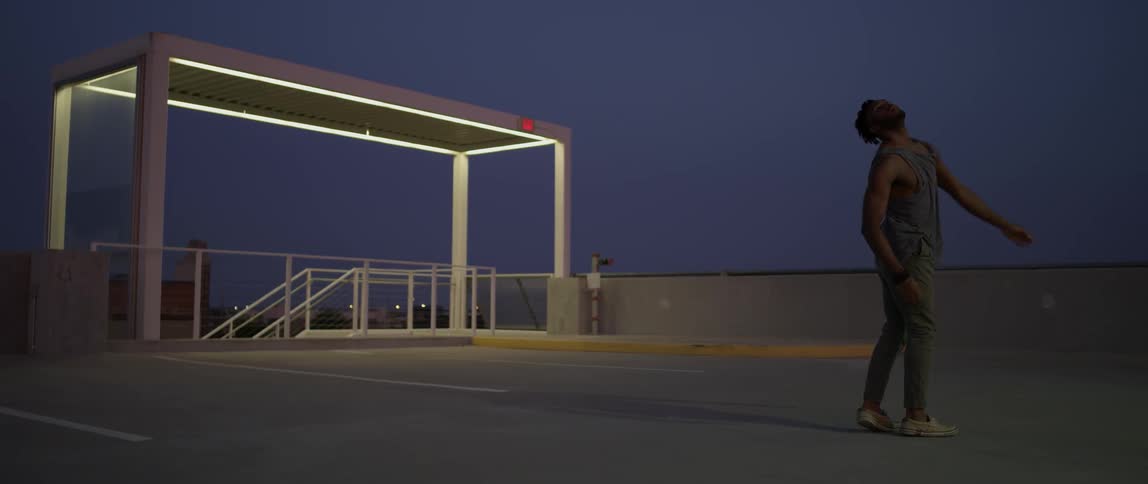 A man is dancing around on the roof of a parking garage at night