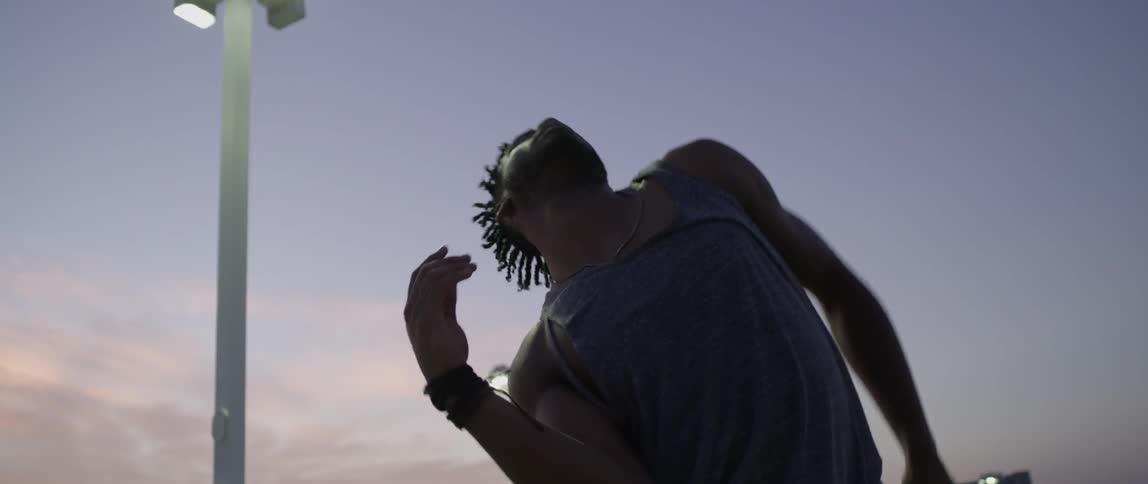 A man is dancing at dusk outside in a parking lot