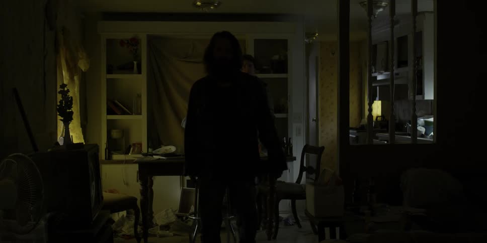 A man enters the house and walks past two people at the table