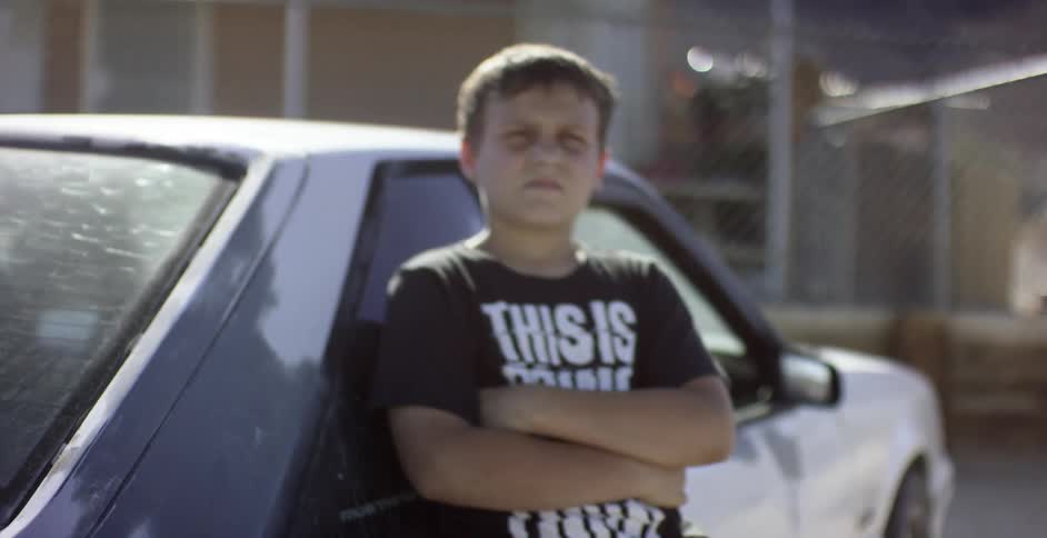 A boy leans against a car on a sunny day