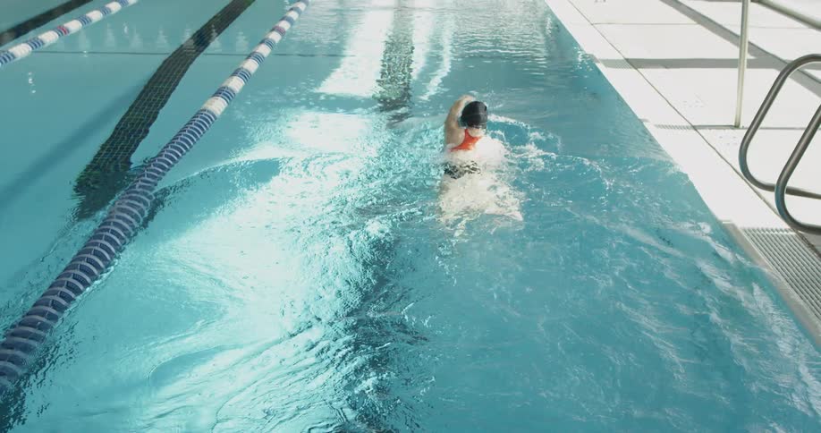 A woman is swimming laps at an indoor pool during the day