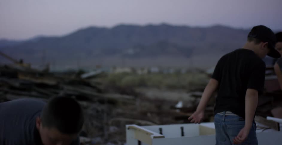 Boys are picking up wood boards from a trash heap at dusk