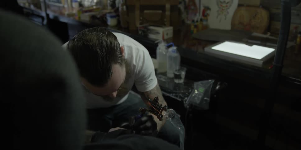 A bearded man tattoos another man