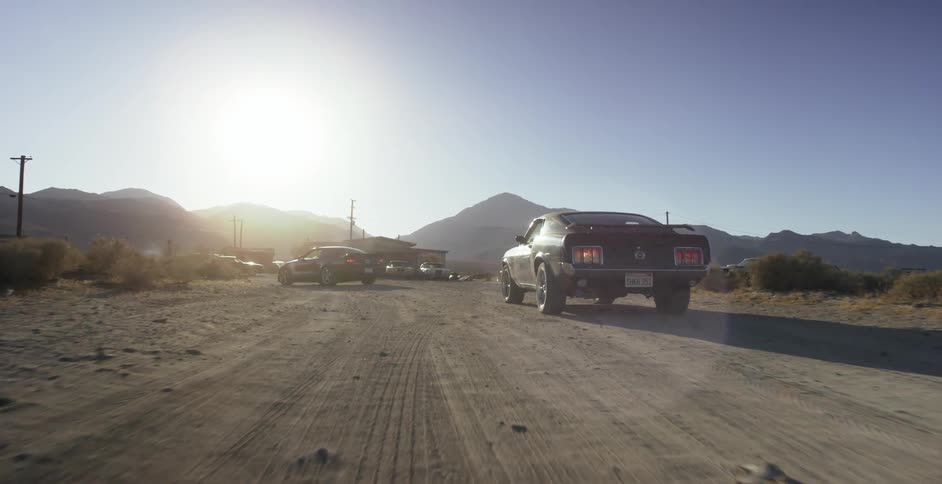 Cars drive down a dirt road into a parking lot