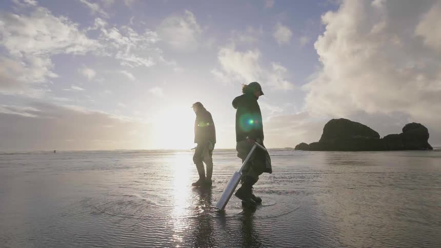 A man is carrying a sand digger across the beach