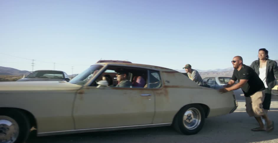 Men push an antique car on a dirt road