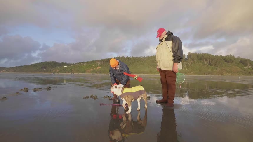 A man pets a kneels down and pets his dog while another man watches