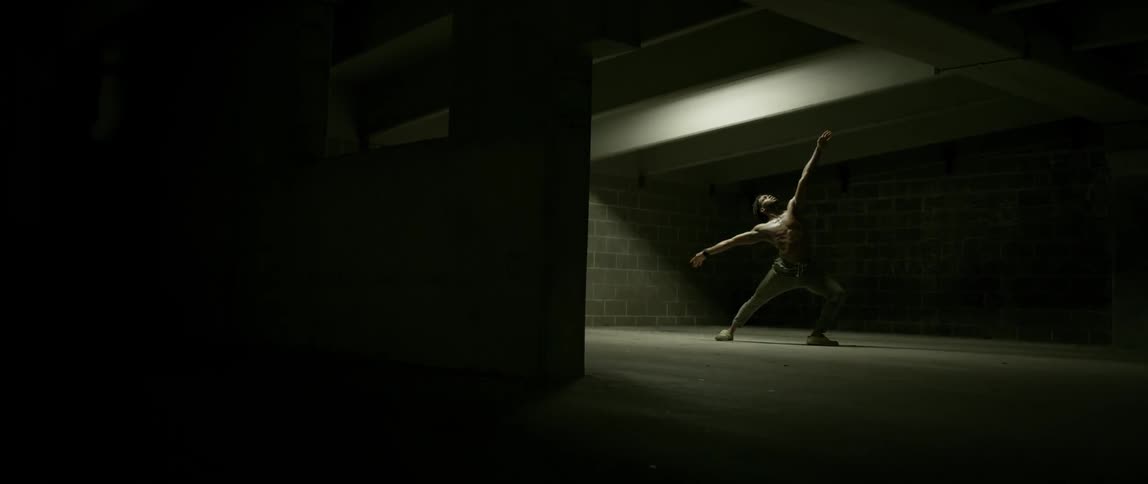 A black man dances in a dim concrete room