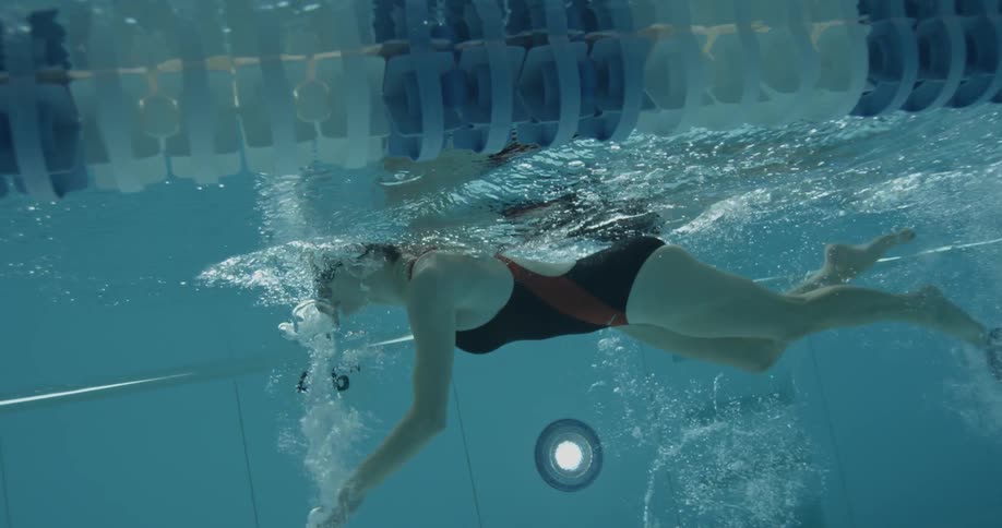 A woman is swimming underwater past a camera