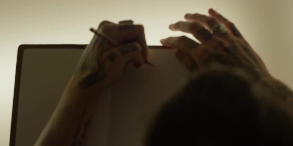A person with tattooed hands writes in a notebook