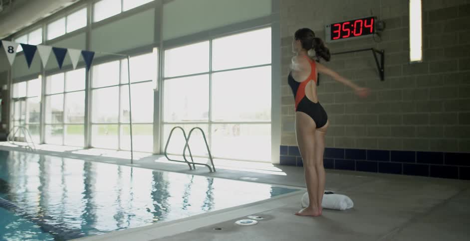 Woman in swimsuit stands stretching at the edge of a pool