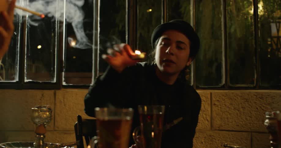 A group of friends are sitting around a table drinking beer and smoking a hookah