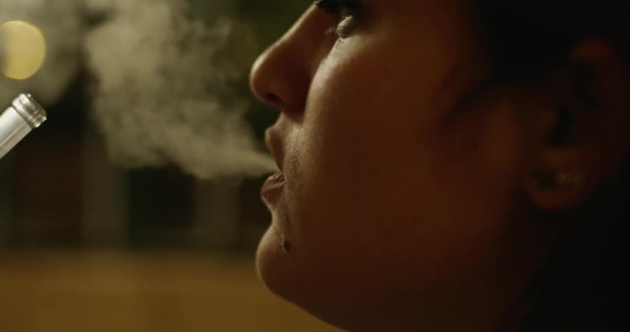 Woman inhales smoke from a pipe and then exhales
