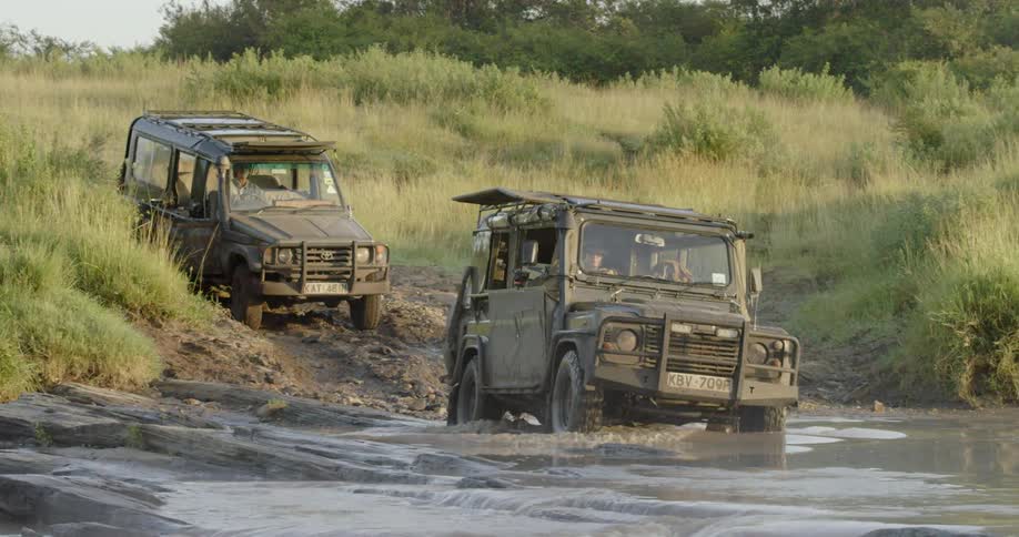 Two jeeps drive into a shallow stream