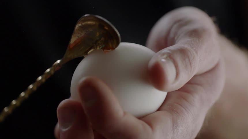 A person cracks an egg open with a small spoon