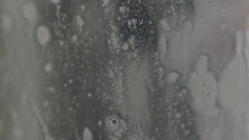 Suds and bubbles drip down a glass surface