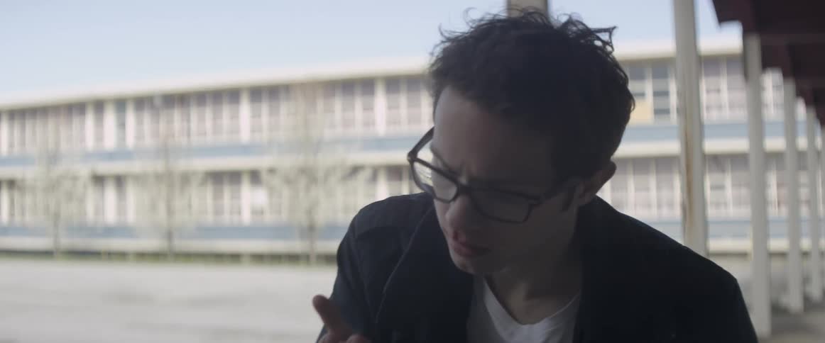 A man is sitting near a building touching his bloody nose