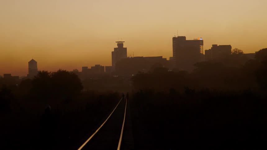 Railroad tracks lead to city buildings at sunset