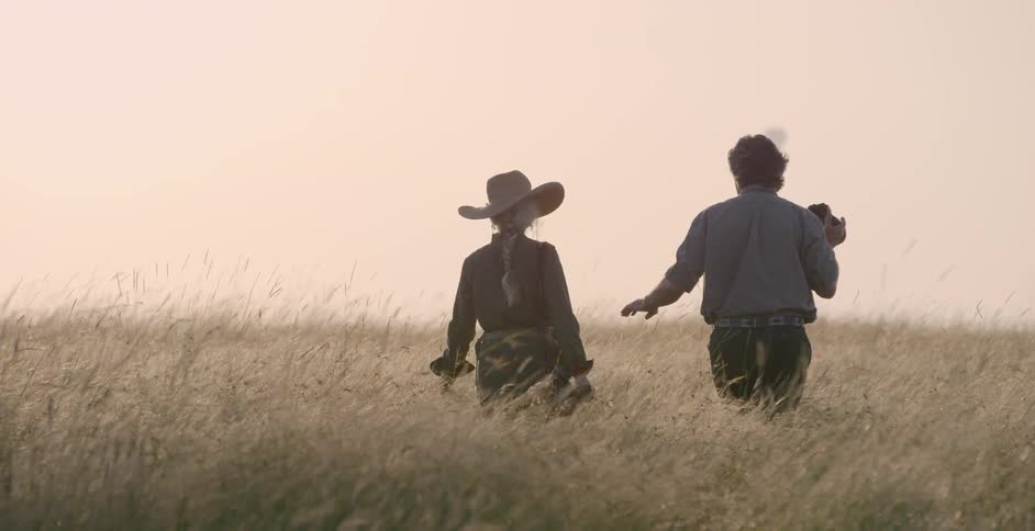 Man and woman hold hands walking through tall grass