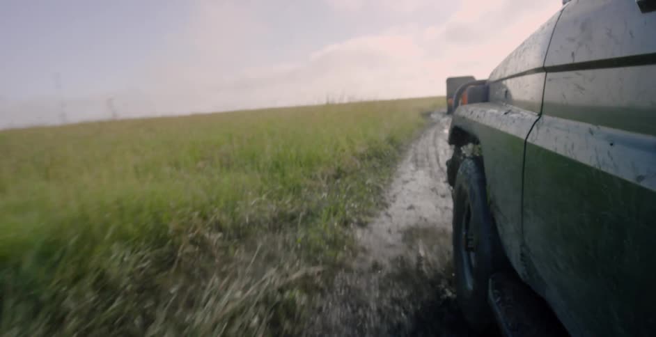 A vehicle drives through mud in a rural field