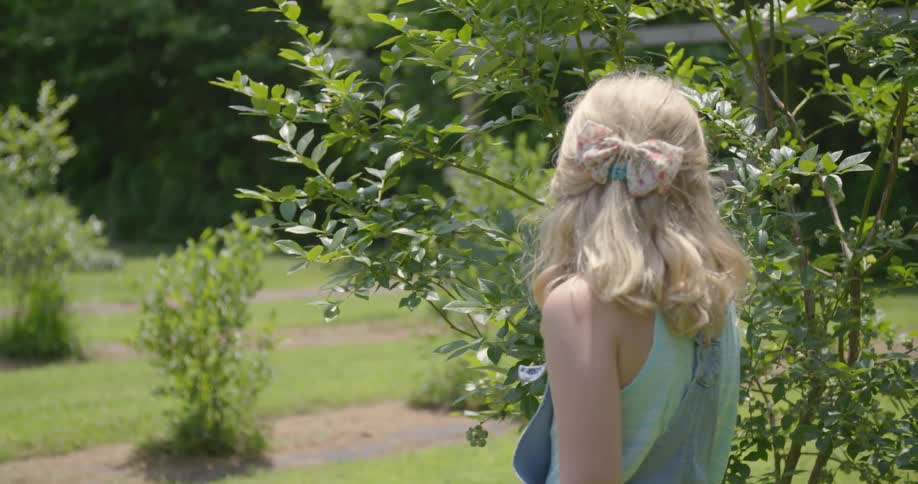 A woman is looking at a bush in her garden