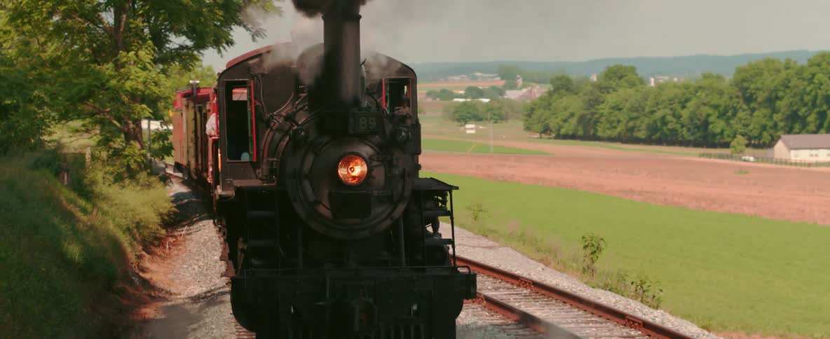 A coal burning train is going in reverse down the tracks