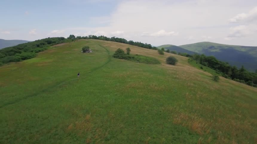Someone is walking through a dirt path on a lush green hill