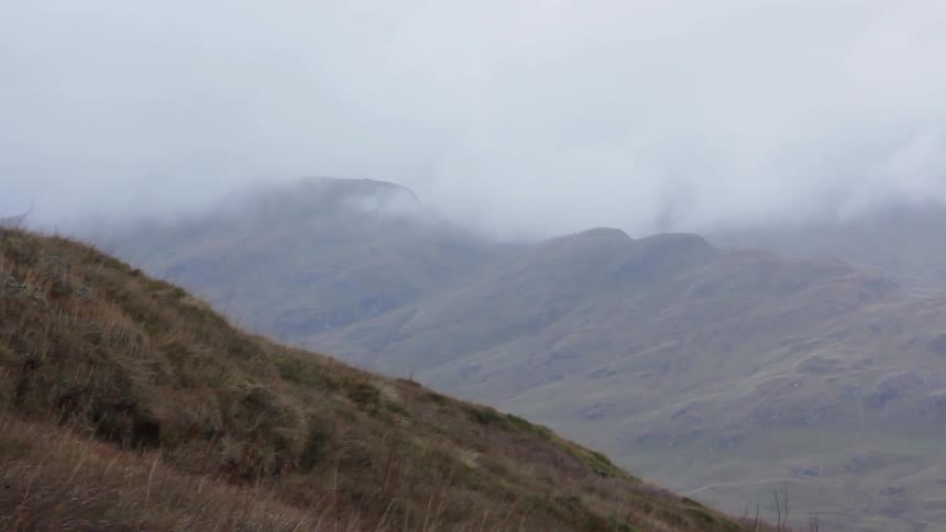 Clouds and mist move across a hilly and mountainous landscape on a breezy day