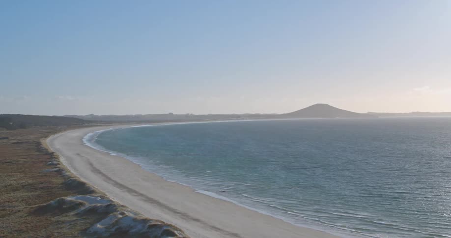 Waves are lapping the shore of a remote beach on a sunny day