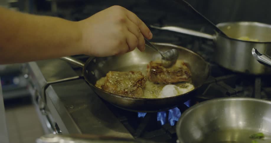 A chef is cooking a meat dish on a stove in a kitchen