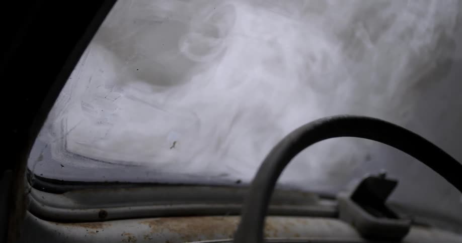 Smoke is pouring from the hood of a stripped old car