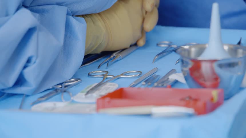 A doctor is leaning on a tray of surgical implements