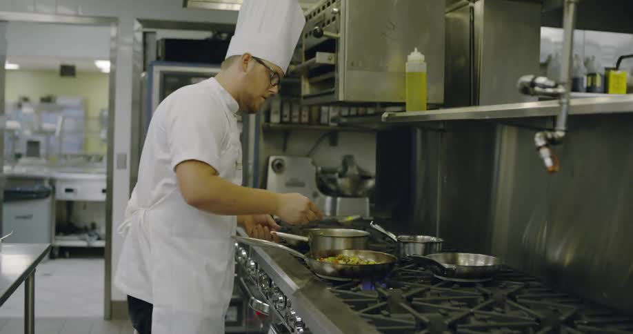Cook flipping food in pan on stove in restaurant kitchen